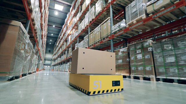 Industrial robot is riding along the storehouse with a box