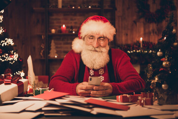 Photo of santa claus sit workspace take delivery service order phone wear hat sweater in north pole office indoors