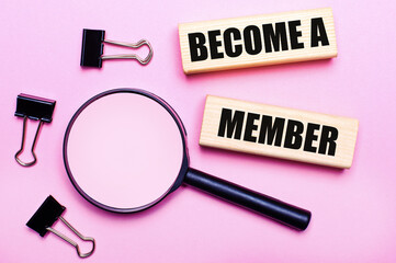 On a pink background, a magnifier, black paper clips and wooden blocks with the text BECOME A MEMBER. Business concept