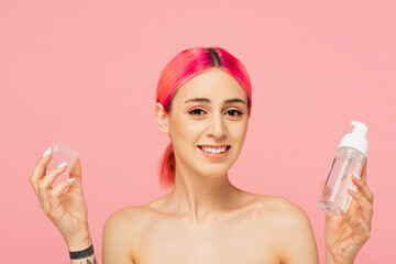 tattooed and happy young woman with colorful hair holding bottle with toner isolated on pink