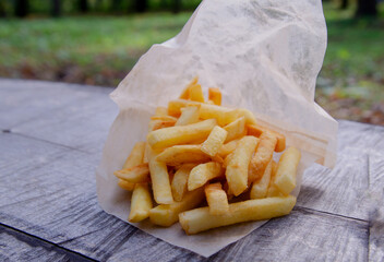 French fries in a paper bag on a wooden background. Eating in the park in nature