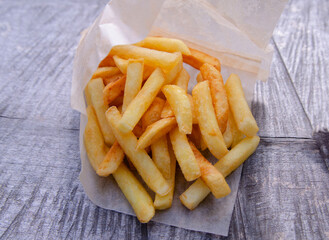 French fries in a paper bag on a wooden background. Eating in the park in nature