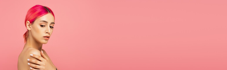 Fototapeta premium pretty young woman with colorful hair touching bare shoulder isolated on pink, banner