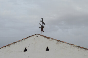 iron weather vane in the shape of a horse with arrow on a roof with sky background