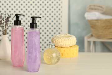 Bottles of shower gel and sponges on wooden table in bathroom