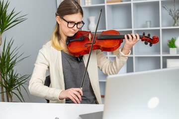 Girl musician doing violin lessons remotely at home using a laptop.