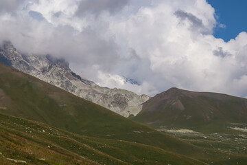 A panoramic view on high Caucasus mountains in Georgia. There are high, snowcapped peaks in the back. Lush pasture in front. Idyllic landscape. Thic clouds above the sharp peaks. Natural remedy