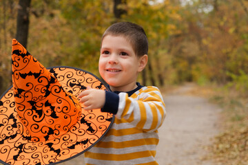 A boy in a striped jacket holds a large orange hat with bats.