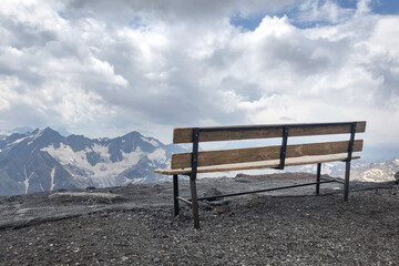 Naklejka na ściany i meble Old wooden bench on top of high winter mountain, cloudy sky on background, copyspace. Place for relaxation in mountains