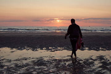 A rear view of a lady walking at the beach enjoying the scenic sunset
