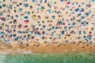 Drone shot of many people enjoying the beach and the ocean in high season- vacation pattern.