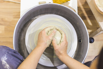 Fototapeta premium Female pottery artist hands shapes the clay on pottery wheel. Creative handmade craft.Top view. Ceramic art studio.