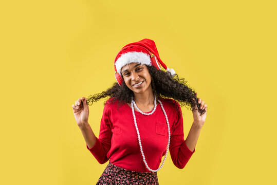 Mujer afroamericana con ropa navideña agarrando su cabello rizado en fondo amarillo