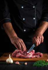 The chef cuts meat with a knife in the kitchen prepares food. Vegetables and spices on the kitchen table in restaurant to prepare a delicious lunch