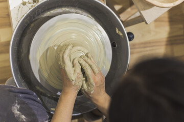 Female pottery artist hands shapes the clay on pottery wheel. Creative handmade craft.Top view. Ceramic art studio.
