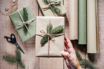 Hand holding stylish eco friendly gift box wrapped in craft paper and decorated with fir tree branch