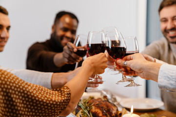Multiracial happy friends drinking wine during thanksgiving dinner