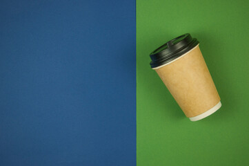 a disposable paper cup of coffee is lying on green and blue background
