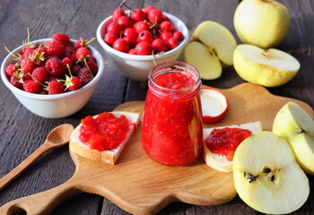 Glass jar with different kinds of berry and fruit on wooden table. Apple, raspberry, hawthorn jam
