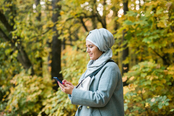 Pretty muslim woman using mobile phone outdoor. Arabic female wearing hijab using smartphone. Islamic girl texting a message phone in city park. Copy space