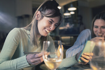 Friends at cinese restaurant. Best friends having a funny conversation eating at fusion food restaurant watching content on the smartphone.