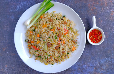 fried rice with spring onions on the white plate and sauce chili on a black background
