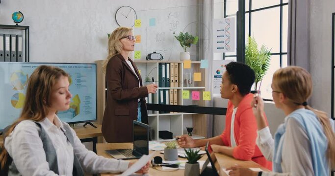 Ambitious business woman draws a graph on glassboard with stickers during a presentation in conference room.