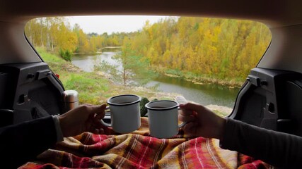 travel, tourism and camping concept - view to river from car trunk with couple under blanket toasting tea cups