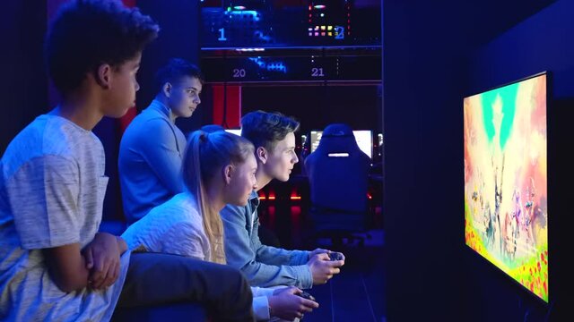 Group of young multiethnic diverse teen sit in cybercafe use pc play on-line video game in dark room. E-sport online competitions event, modern tech, gen z addict with virtual games concept