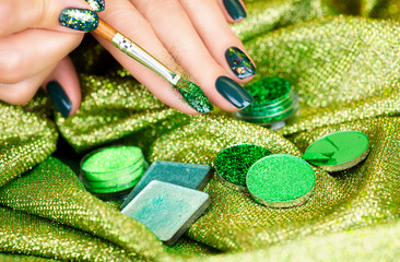 Festive manicure. Green manicure with sparkles on a shiny background. Female hand with a beautiful green manicure.