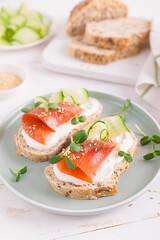 Fototapeta na wymiar Toasts or open sandwiches with salted salmon, ricotta cream cheese, cucumber, sprouts and whole grain bread on white table. Healthy food, diet. Breakfast.
