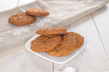 Several sweet oatmeal cookies with a ceramic saucer and a linen napkin, close-up, on a wooden table.