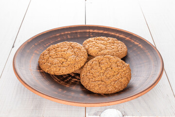 Several sweet oatmeal cookies with ceramic dishes, close-up, on a wooden table.