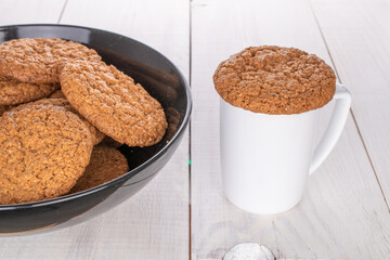 Several sweet oatmeal cookies with ceramic dishes, close-up, on a wooden table.