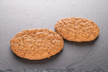 Two sweet oatmeal cookies, close-up, on a slate stone.