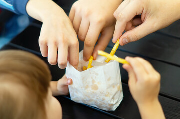 Teenagers take French fries from their younger sister. The family is having lunch at a fast food cafe. The family eats French fries together. Friends Eat French Fries. Photo of people sharing potatoes