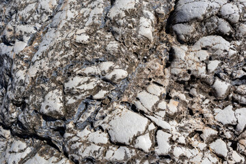 White and black big marble rock material with cracks close-up texture. Light stone surface pattern details in sunny Greece