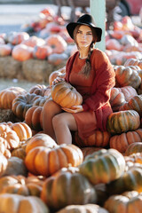 Portrait of happy woman with ripe orange pumpkin in hands on background of farmers market in brown sweater and hat. Cozy autumn vibes Halloween, Thanksgiving day.