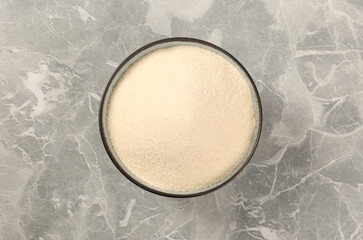Uncooked organic semolina in bowl on grey table, top view