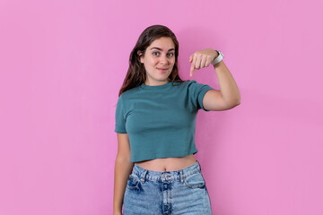 Young woman pointing downward and looking at camera, on pink banner background with copy space.