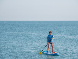 Naklejka premium Paddle boarder. Sportsman paddling on stand up paddleboard. SUP surfing. Active lifestyle. Outdoor recreation. Vacation on seaside.
