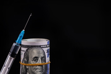 Disposable syringe and 100 american dollar bills on black background