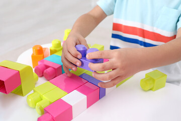 Little child playing with colorful building blocks at table indoors, closeup