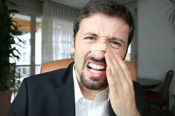 Young elegant man touching broken nose with adhesive bandage plaster