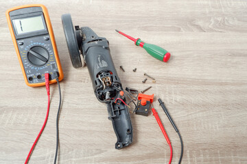 Power tool repair. Angle grinder disassembled for repair on the table. Screwdriver, multimeter.