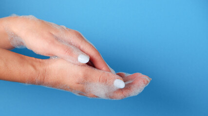 Bubble bath foam in woman's hands. Closeup woman's hand washing with soap on a blue background ,...