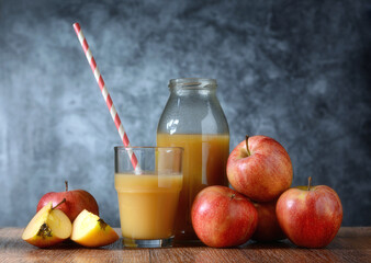 apple juice in the glass with drinking straw - fruit around - gray background - closeup