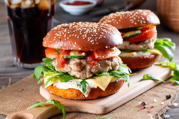 Tasty grilled homemade burgers with beef, tomato, cheese and arugula on wooden background. Fast food and junk food concept.