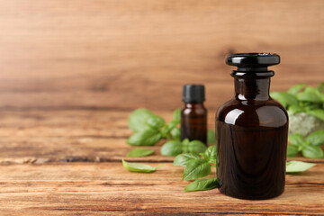 Glass bottles of basil essential oil and leaves on wooden table, space for text