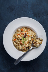 Risotto, Italian rice with mushrooms, vegetables and parsley served on white porcelain plate